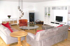 Ein Wohnzimmer mit einem grauen Sofa, einem runden Couchtisch, einem roten Sessel, einem Fernseher und einer weißen Vitrine mit Glastüren.