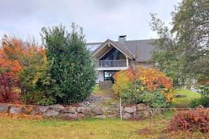 Ein modernes Haus mit einer Steinschmalseite, einer Holzterrasse und einem großen Baum im Vordergrund.