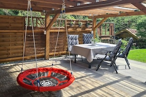 Eine Terrasse im Freien mit einer Schaukel, einem Tisch mit Stühlen und einem Holzzaun im Hintergrund.