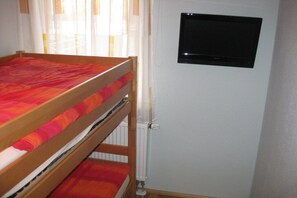 A bunk bed with a red and orange bedding, a white radiator, and a black television mounted on the wall. - on the dike in Grimmershörn Bay (Cuxhaven)