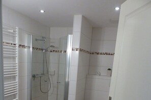 Ein modernes Badezimmer mit einer Duschkabine aus Glas, weißen Fliesen und einem kleinen Regal mit einer Pflanze.