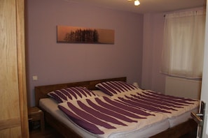 Ein Einzelbett mit gestreifter Bettdecke, ein Nachttisch, ein Wandbild und ein Fenster mit Vorhängen.