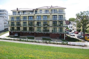 A multi-story residential building with balconies, a parking area, and a grassy field in the foreground. - on the dike in Grimmershörn Bay (Cuxhaven)