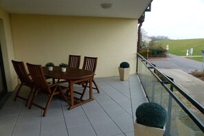 Ein Balkon mit Holztisch und -stühlen, Blumentöpfen und Blick auf eine Straße und Grünflächen.