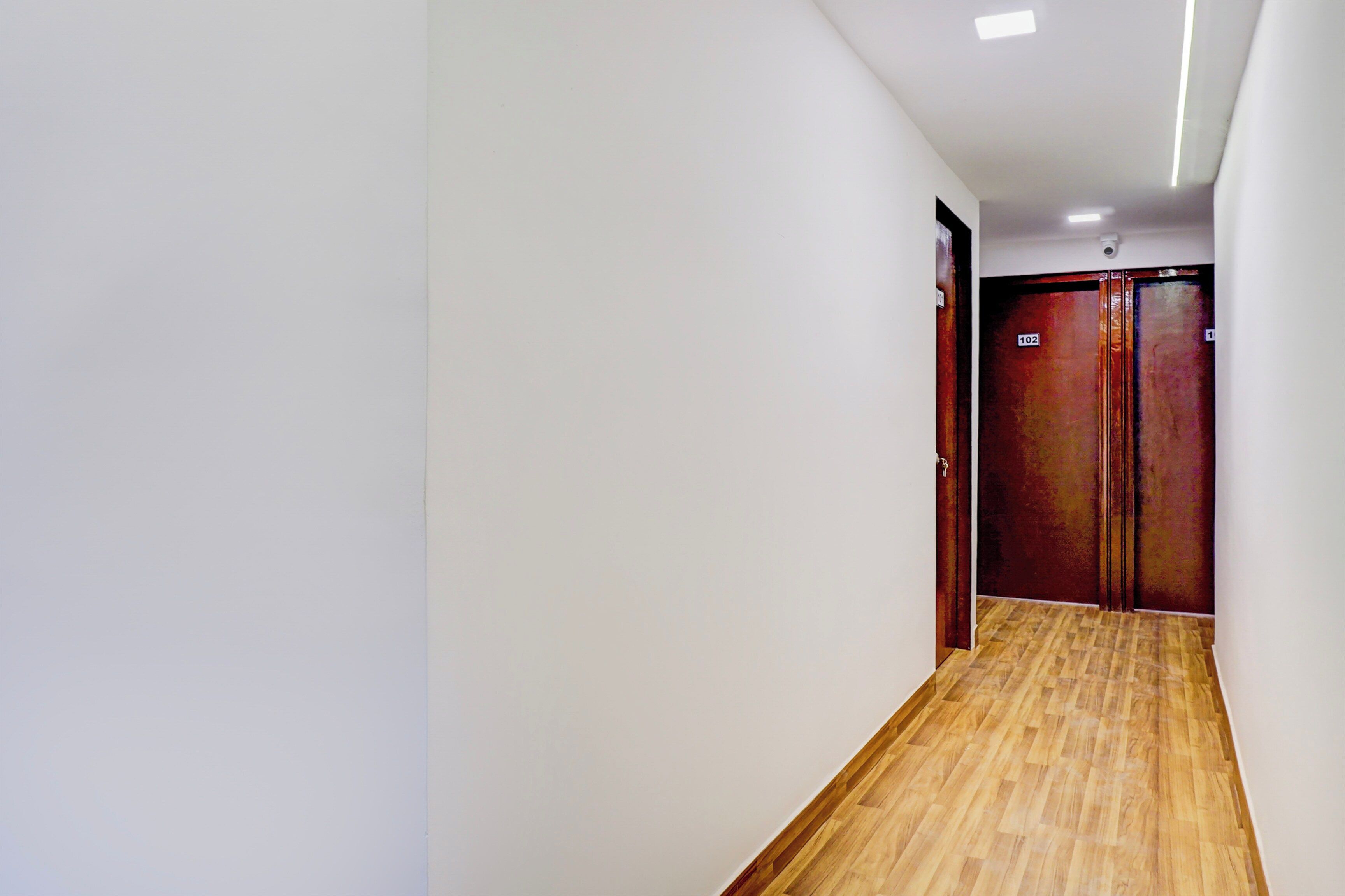 A hallway with wooden flooring, white walls, and two doors with a number sign.