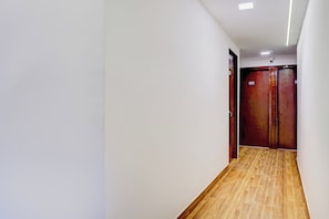 Un pasillo con suelo de madera, paredes blancas y dos puertas con un letrero de número.