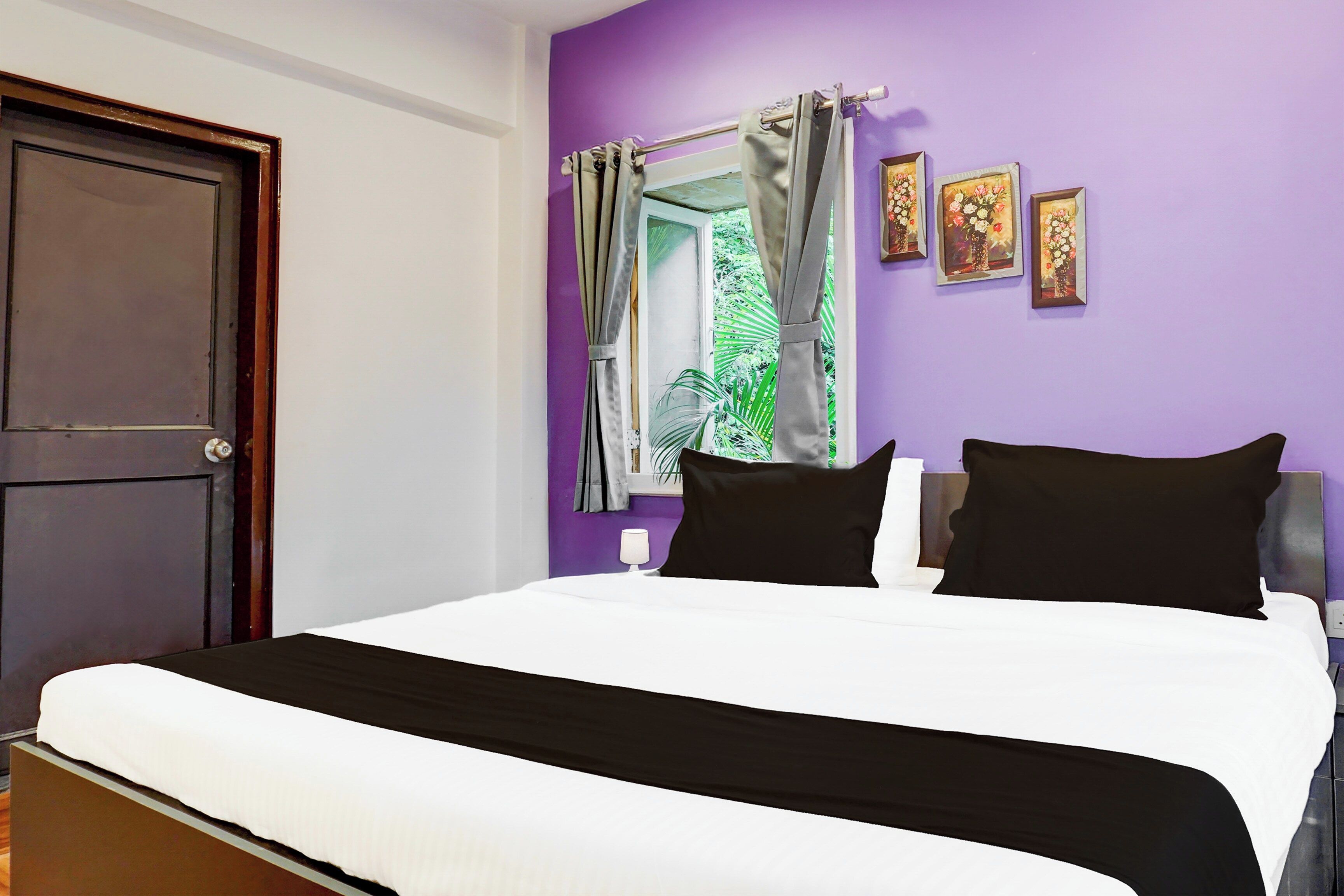 Quarto com cama, janela com cortinas e obras de arte nas paredes.