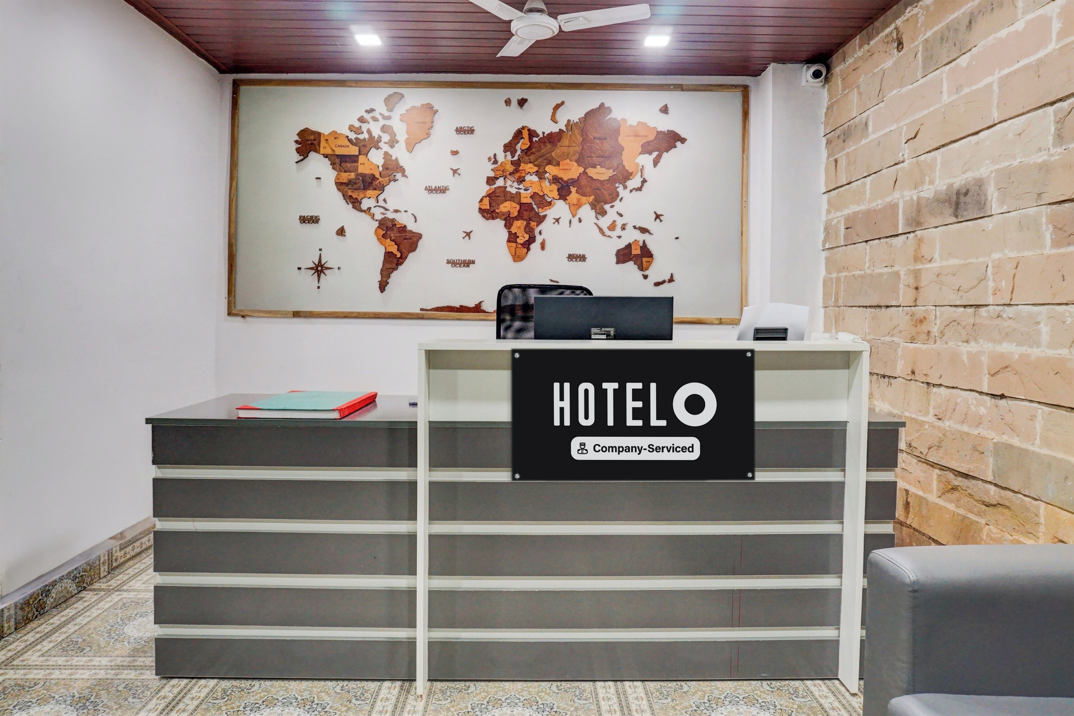 Una mesa de recepción con un mapa mundial, un letrero que indica 'HOTEL Company Serviced' y una lámpara de escritorio pequeña.