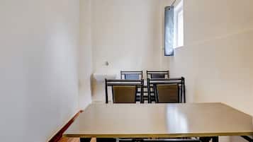 Una habitación con una mesa larga, cuatro sillas, un lavamanos blanco y una ventana con cortina.