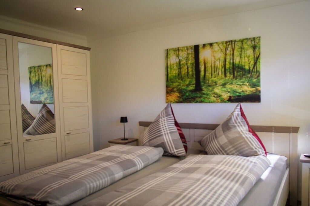 Quarto com cama, mesa de cabeceira, espelho e pintura de uma floresta na parede.