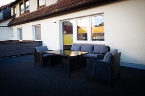 An outdoor seating area with a table and two chairs, a sofa, and a window with a view of a building. - Holiday apartment with 2 bedrooms (Bad Sachsa)