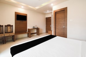 Habitación de hotel con cama, escritorio, silla, televisor y armario.