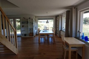 A room with a wooden floor, a dining table with chairs, a bookshelf, and a window with curtains. - Holiday home in Buren with swimming pool (Buren)