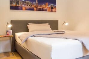 A neatly made bed with a gray headboard, two bedside lamps, and a framed cityscape picture above. - Holiday apartment with 2 bedrooms (Detmold)