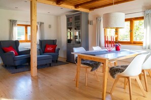 Een moderne woonkamer met een eethoek, houten balken, een kast en een raam met gordijnen.