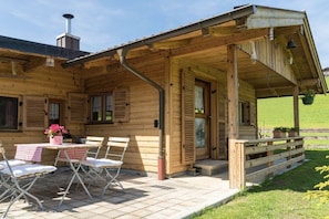 A wooden cabin with a covered patio, a table with chairs, and a potted plant. - Alpenchalet Sachrang (Aschau im Chiemgau \/ Sachrang)
