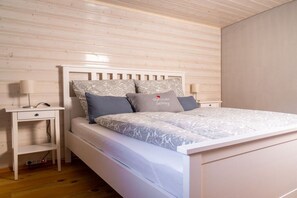 A bedroom with a white bed, a nightstand, a lamp, and a wall with horizontal wooden planks. - Alpenchalet Sachrang (Aschau im Chiemgau \/ Sachrang)