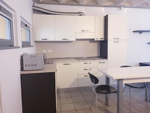 A compact kitchen with white cabinets, a small countertop, and a dining area with a table and chairs. - Appartamento moderno con parchieggio  (Lecco)