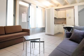 A compact living space with a sofa, a small table, a kitchenette, and a radiator. - Appartamento moderno con parchieggio  (Lecco)