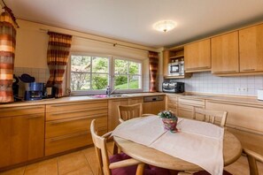A kitchen with wooden cabinets, a dining table with chairs, a window with curtains, and a microwave.