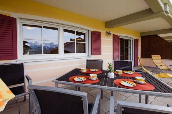 A dining area with a table set for four, outdoor chairs, and a view of mountains through the windows.