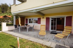 A covered patio with a table and chairs, a striped lounge chair, and a sliding glass door.