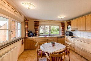A kitchen with wooden cabinets, a dining table with chairs, a window with curtains, and a microwave.