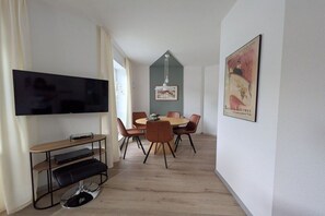 A modern living room with a flat-screen TV, a dining table with chairs, a wooden coffee table, and a framed picture on the wall. - Holiday apartment with 1 bedroom (Füssen)