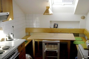 A compact kitchen with a wooden table, a white chair, a stove, and a hanging light fixture. - Holiday apartment with 1 bedroom (Oy-Mittelberg)