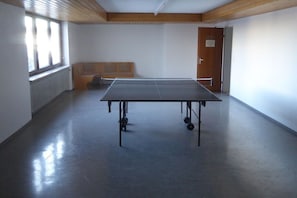 Et bordtennisbord i et rum med træloft, en radiator og en dør.
