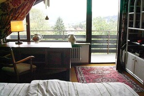 Una habitación con cama, escritorio con lámpara, un florero y vistas al exterior a través de una ventana.