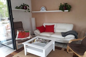 A living room with a white sofa, red cushions, a glass coffee table, and a brown armchair. - Holiday apartment with 1 bedroom (Schneverdingen)