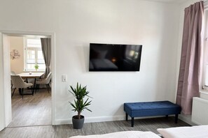 A modern living room with a flat-screen TV mounted on the wall, a blue bench, a potted plant, and a dining area visible through an open doorway. - Holiday apartment with 2 bedrooms (Wernigerode)