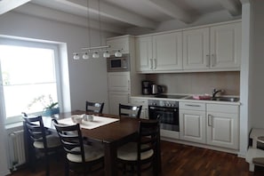 A modern kitchen with white cabinets, a dining table with chairs, a built-in oven, and a coffee maker. - Holiday home with 3 bedrooms (Greetsiel)