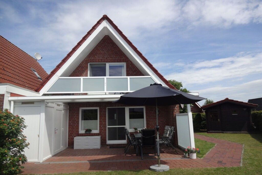 Une maison à deux étages avec une façade en briques, une fenêtre à cadre blanc, un patio avec une table et des chaises, et un parasol noir.