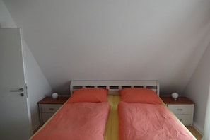 Een slaapkamer met twee eenpersoonsbedden, elk voorzien van een kussen en een nachtkastje met een lamp.