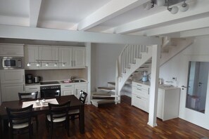 Een moderne keuken met witte kastjes, een eethoek met een houten tafel en stoelen, en een trap naar een hoger gelegen verdieping.