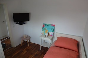 A bedroom with a bed, a television mounted on the wall, a small table with a decorative item, and a door leading to another room. - Holiday home with 3 bedrooms (Greetsiel)