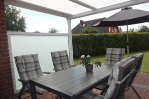 An outdoor patio with a table and chairs, a potted plant, and a large umbrella. - Holiday home with 3 bedrooms (Greetsiel)