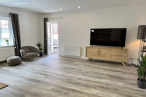A living room with a flat-screen TV, a sofa, a wooden cabinet, and a potted plant. - Holiday apartment with 3 bedrooms (Wernigerode)