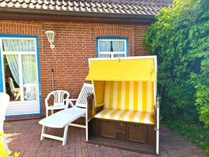 A patio area with a yellow and white striped bench, white chairs, and a table. - Holiday Apartment With 1 Bedroom (Wyk auf Foehr)