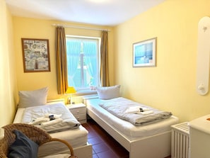 Ein Hotelzimmer mit zwei Betten, einem Fenster mit Vorhängen, einem Heizkörper und einem gerahmten Bild an der Wand.