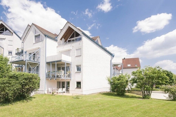 Ein mehrstöckiges Wohngebäude mit Balkon, überdachter Außenbereich und gepflegtem Rasen.