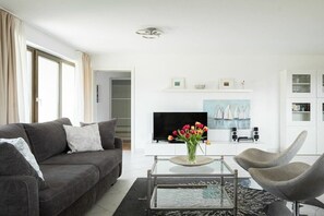 Una sala de estar moderna con un sofá, sillones, una mesa de centro y un televisor de pantalla plana.