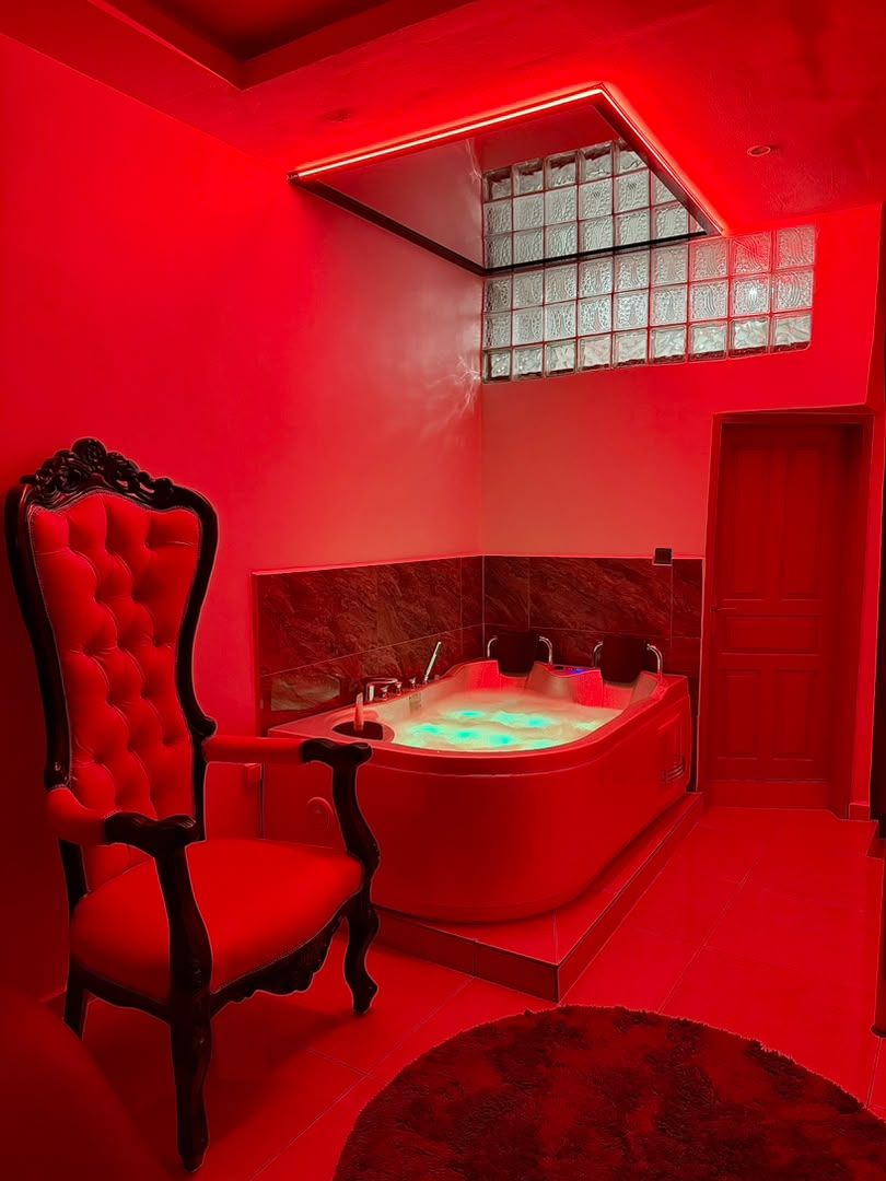 Een rode badkamer met een groot bad, een rode stoel en een raam met gezandstraald glas.