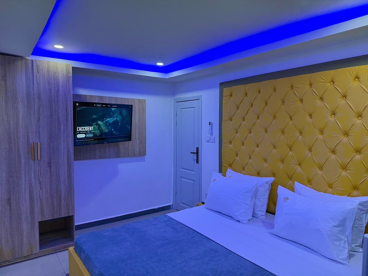Un dormitorio con una cama, televisión instalada en la pared, un armario y una puerta.