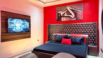 A modern bedroom with a large bed, a mounted TV, and a red accent wall.