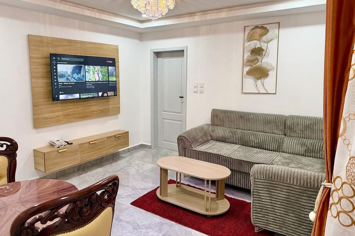 Een woonkamer met een flatscreen televisie aan de muur, een grijze bank, een houten salontafel en een rode vloerkleed.
