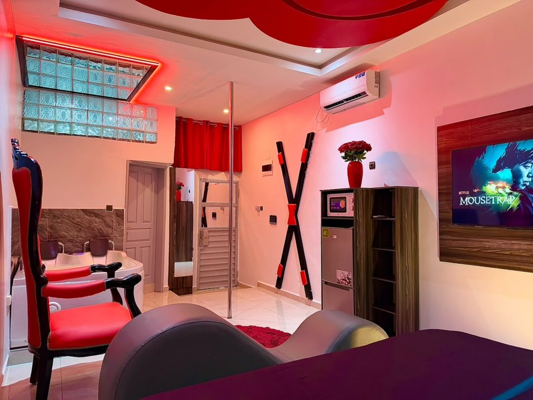 A modern living room with a TV, a dining area, and a red accent wall.