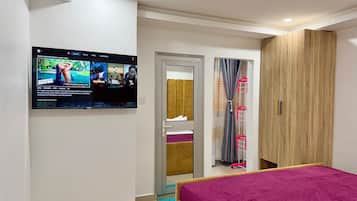 A bedroom with a bed, a TV mounted on the wall, a wardrobe, and a door leading to a bathroom.